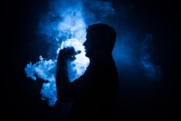Vaping man holding a mod. A cloud of vapor. Black background. Vaping an electronic cigarette with a...