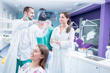 Dental medical team examining and working on young ¸female patient.Dentist's office, while technician is reviewing xray.