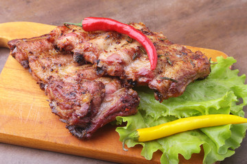 grilled barbecued ribs with lettuce leaves, hot chili pepper and sauce on wooden cutting board.