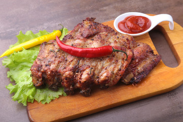 grilled barbecued ribs with lettuce leaves, hot chili pepper and sauce on wooden cutting board.