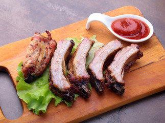 grilled barbecued ribs with lettuce leaves, hot chili pepper and sauce on wooden cutting board.