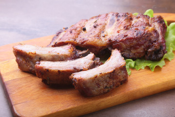 grilled barbecued ribs with lettuce leaves, hot chili pepper and sauce on wooden cutting board.