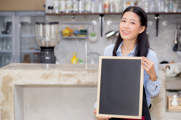 Portrait of beautiful young barista, asian woman is a employee standing holding chalkboard in counter coffee shop, service concept.