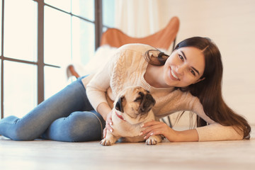 Young woman with cute pug dog near window at home. Pet adoption