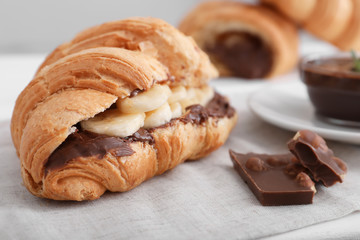Tasty croissant with banana and chocolate sauce on table