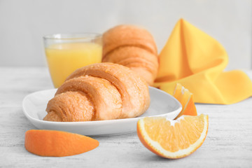 Tasty croissant and slices of orange on table