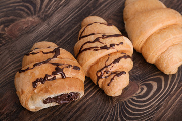 Tasty croissants with chocolate sauce on wooden table