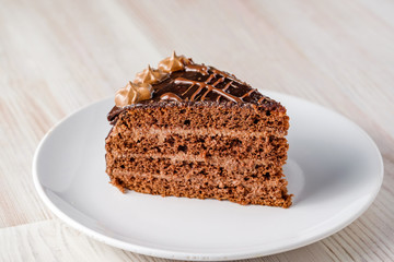 The slice of chocolate cake Prague with chocolate buttercreamy frosting on a white plate. Homemade baking. Close-up view.
