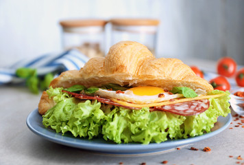 Plate with tasty croissant sandwich on table