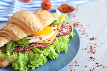 Plate with tasty croissant sandwich on table