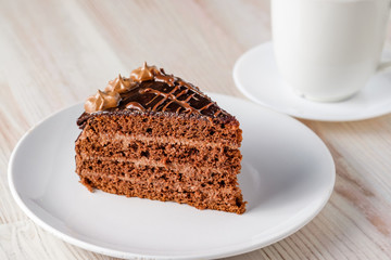 The slice of chocolate cake Prague with chocolate buttercreamy frosting on a white plate. Cup of tea near it. Homemade baking. Close-up view.