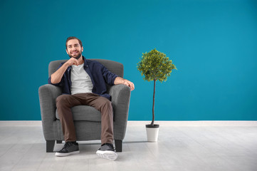Handsome man sitting in comfortable armchair against color wall
