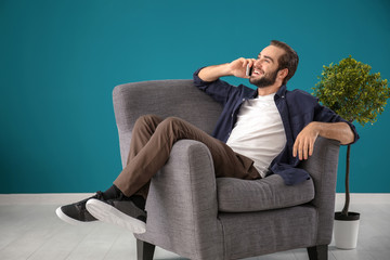 Handsome man talking on mobile phone while sitting in comfortable armchair at home