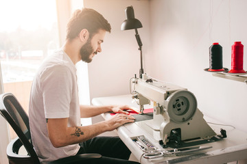 Young stylish man with tattoo tailor working on new clothing