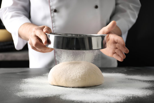 Man sifting flour over dough on table