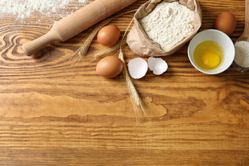 Wheat flour, eggs and kitchen utensils on wooden background