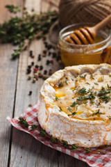 A real Camembert from France with thyme, honey and toasted bread on old wooden rustic table. Soft cheese on a wooden background. Top view