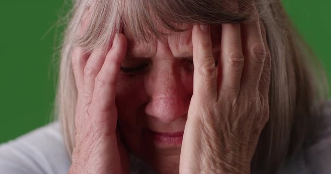 Tight shot of elderly woman with migraine headache in front of greenscreen