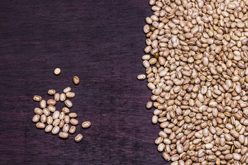 Small portion of Carioca beans on the left side and a lot on the right side on a purple table / Feijão Carioca