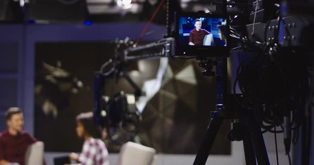 Young confident and relaxed man and woman taking participation in television show sitting in modern illuminated studio and having talk. The cameraman of the TV recording show.