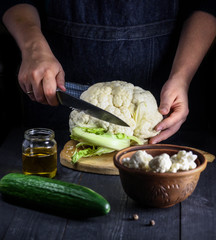 Cut cauliflower with a knife on a wooden board. Hands in the frame.