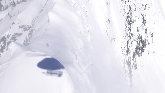 Helicopter flies over skier on mountain ridge, British Columbia