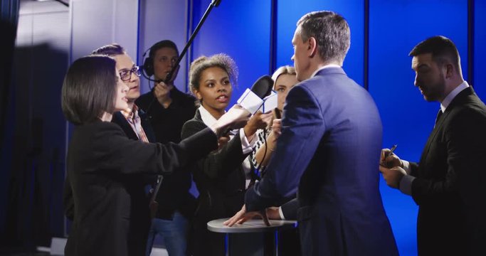 Middle-aged politician in suit talking to group of multiracial journalists having interview and suddenly leaving auditorium without any comment.