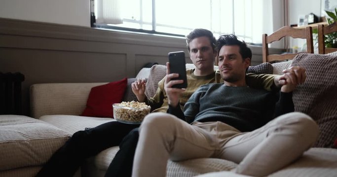 Young male couple relaxing on sofa streaming entertainment