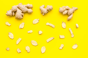 Whole and sliced ginger roots yellow background top view
