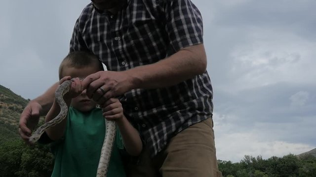 Father shows son a large snake and lets him hold it.