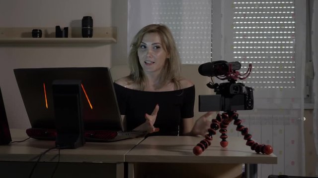 Blonde attractive female video blogger filming herself with a camera at office teaching audience how to analyze traffic data