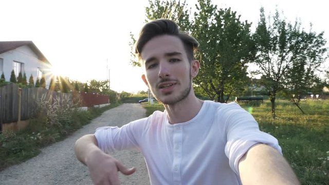 Young man smiling and talking to camera held in hand and recording video for his blog outside in nature on a sunny day