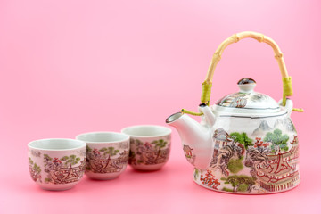 Teapot with cups on a pink background.