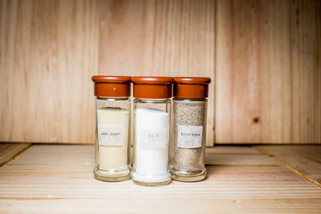 Concept of salt, black and white pepper powder accessories. Bottles with salt, black and white pepper on wooden background. Horizontal.