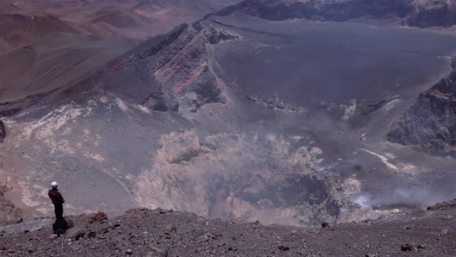 Scientist standing on the edge and looking to the smoked crater. Beautiful horizon of mountains. Aerial view. 4k