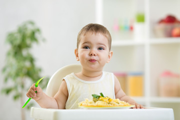 funny baby boy eating healthy food in kitchen