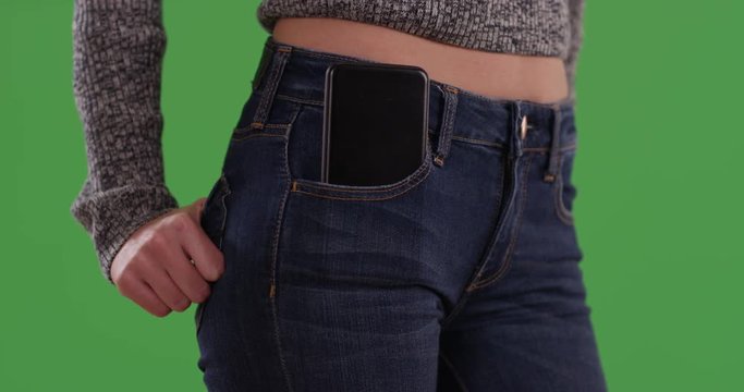 Close up of millennial woman in blue jeans with hands in back pockets and smartphone in front pocket on greenscreen. Close-up mid section of girl with cell phone. 4k on green for keying or compositing