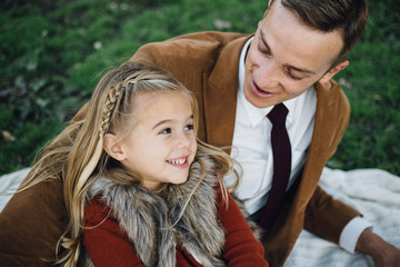 Young girl leaning on her dad who is lying on a blanket outside