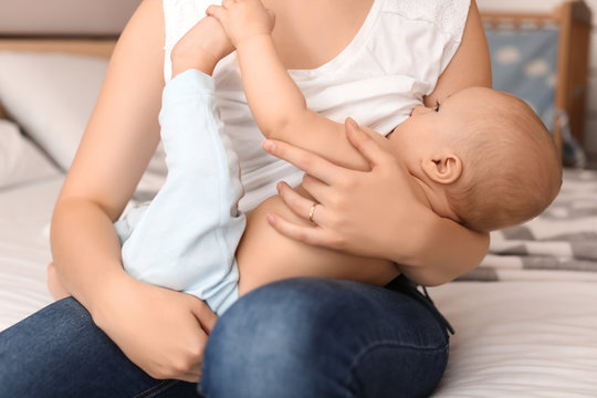 Young mother breastfeeding her little baby on bed at home