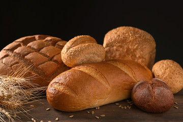 Variety of fresh tasty bread on wooden table against dark background