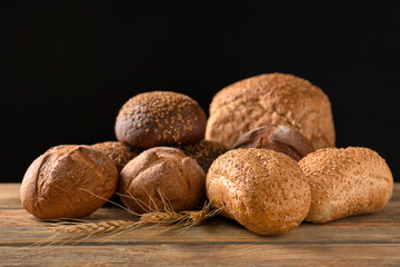 Variety of fresh tasty bread on wooden table against dark background