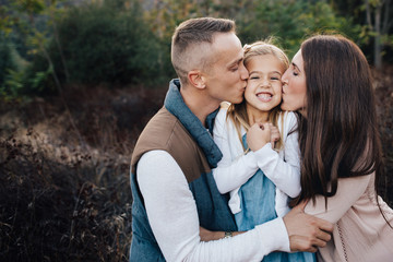 Mom and Dad kissing both cheeks of young daughter.