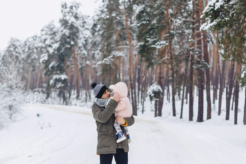 Fototapeta na wymiar the dad holds a small daughter on the snowy picturesque terrain in a pine forest on the highway