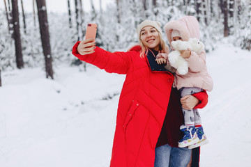 the mom holds a small daughter doing a selfie in the snowy picturesque area of the pine forest on the highway