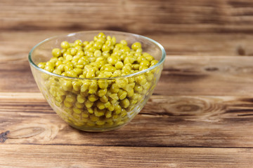 Canned green peas in glass bowl on wooden table