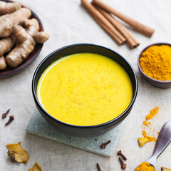 Turmeric drink, tea, milk with cinnamon with fresh and dried turmeric on a textile grey background.