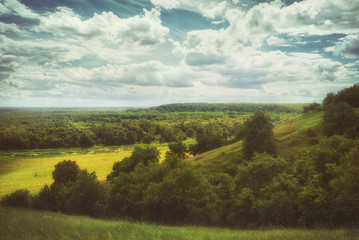 Fields and meadows in a hilly valley under a cloudy summer sky