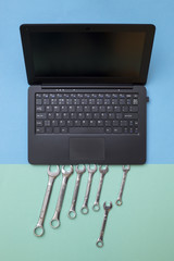 Laptop and seven spanners on a colored background, top view