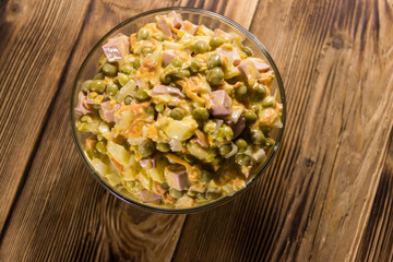 Mayonnaise salad with sausage, green pea, carrot and onion on wooden table