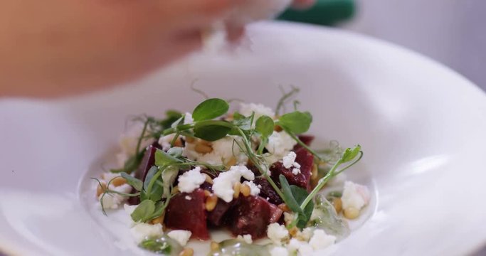 4K Professional chef in restaurant kitchen putting finishing touches to gourmet dish. Close up on hands, no faces can be seen.